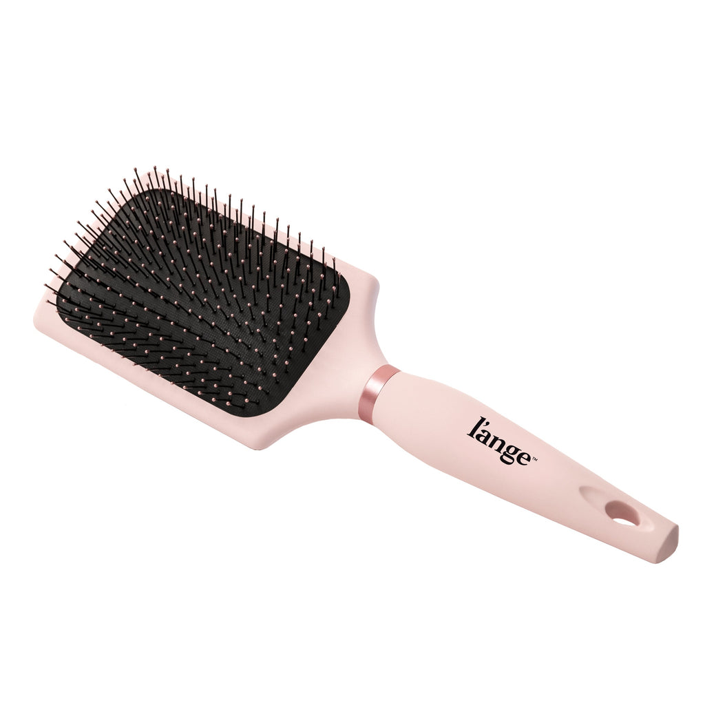 A pink paddle brush sits diagonally in a white background, displaying the logo & cushioned bristles.