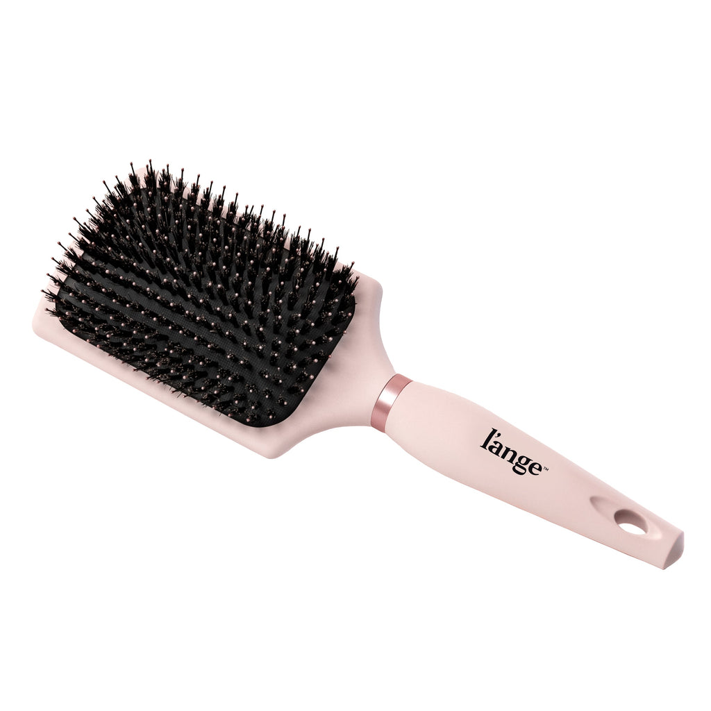The pink boar bristle brush sits diagonally, showing its handle, the logo, and paddle.