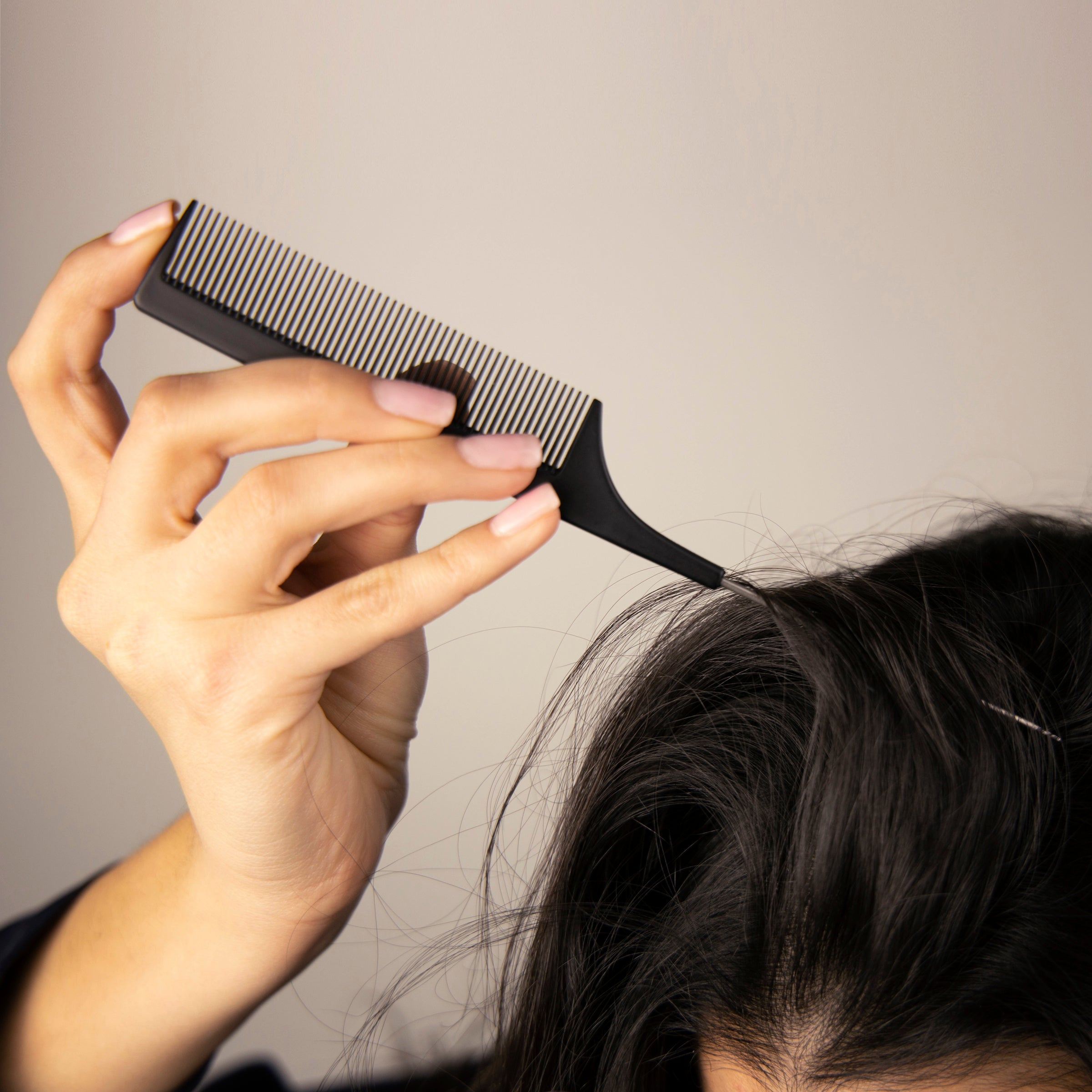 A woman uses the pointed, metal tail handle of the carbon fiber hair comb to separate her hair.