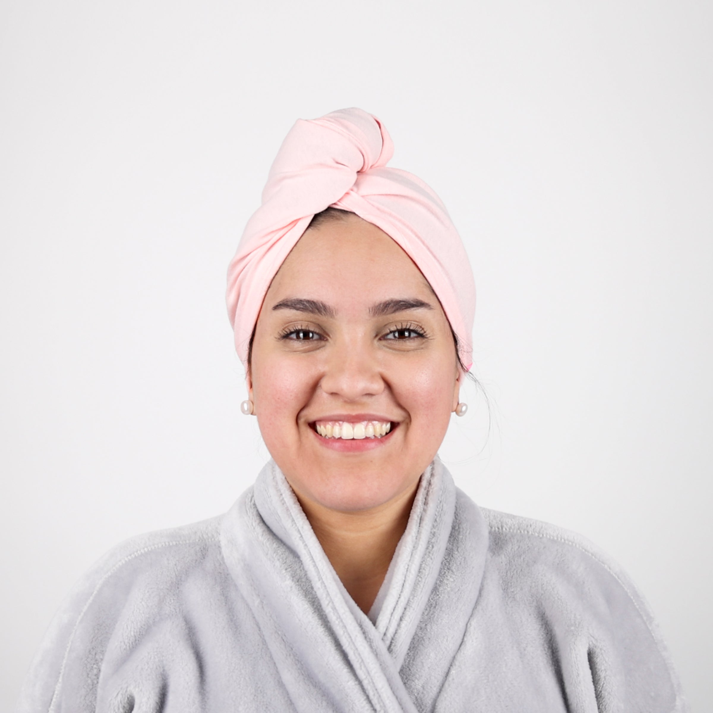 A woman smiles at you while wearing a bathrobe and the pink hair wrap towel.