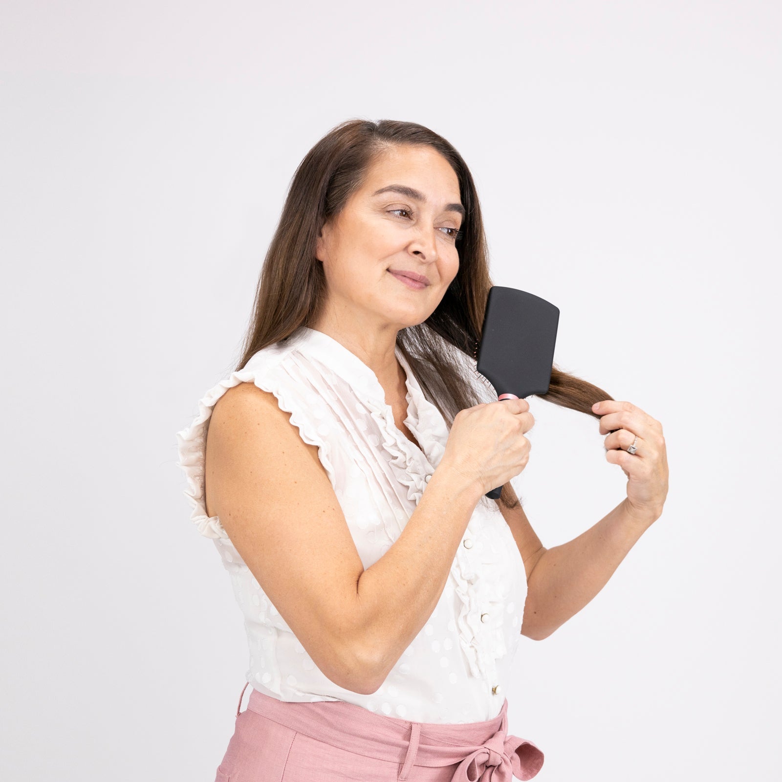 A woman with a contented look and white top brushes her hair with the black Siena Paddle Brush.