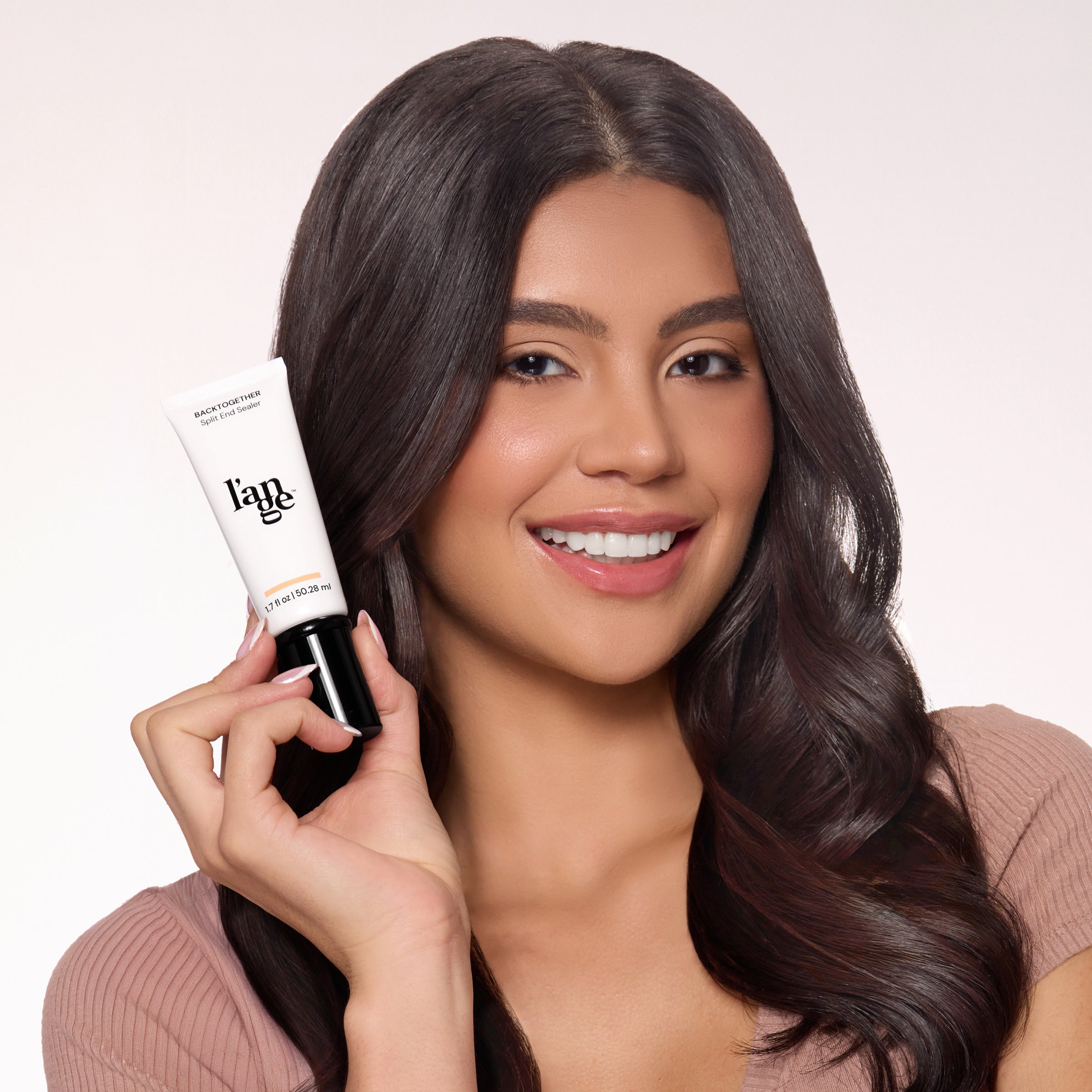 Smiling individual holding a tube of L'ange hair product, showcasing sleek, glossy hair, emphasizing the product's effect.