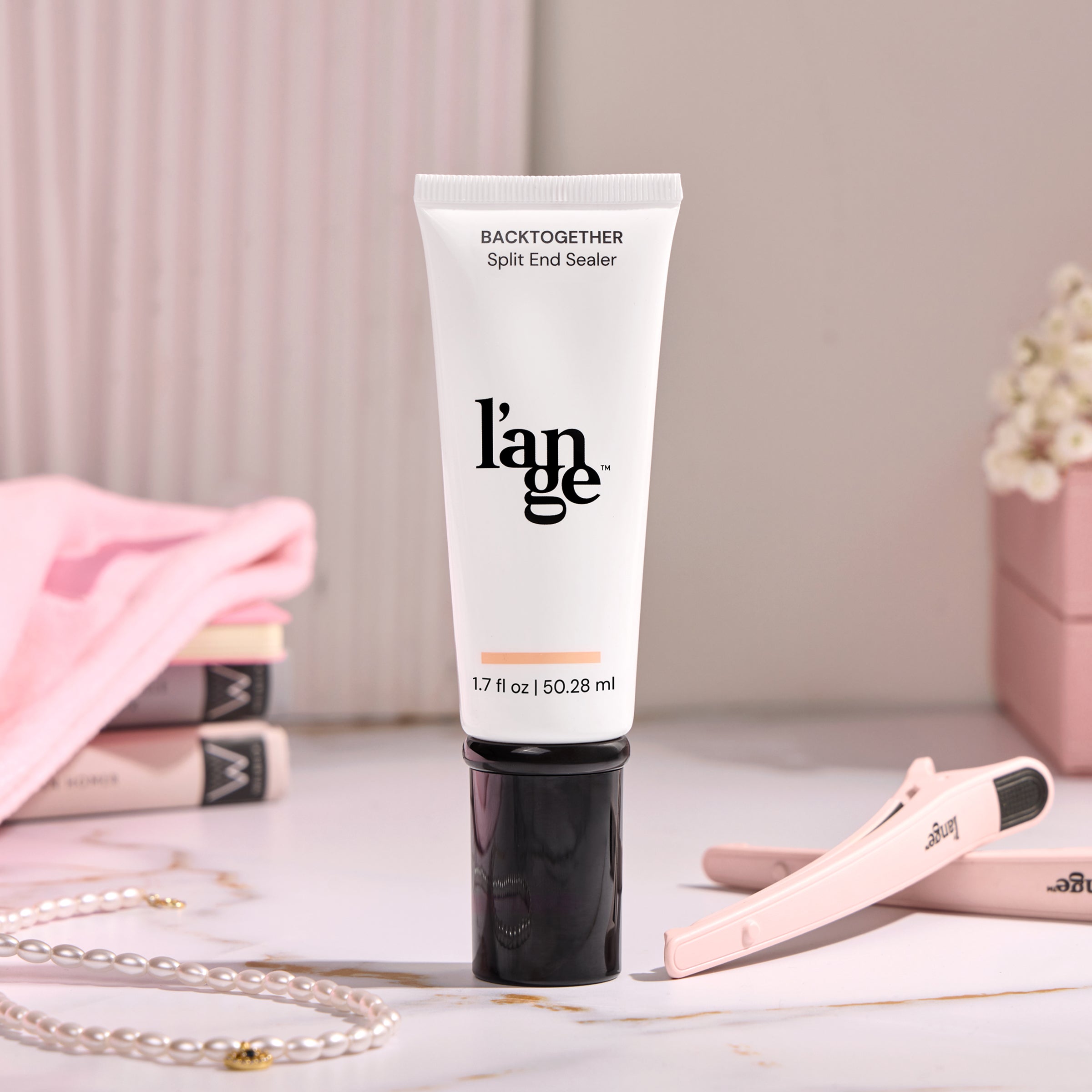 L'ange Back Together Split End Sealer tube, 1.7 fl oz (50.28 ml), on a marble surface with soft pink accents, a hair clip, and a pearl necklace in the background.