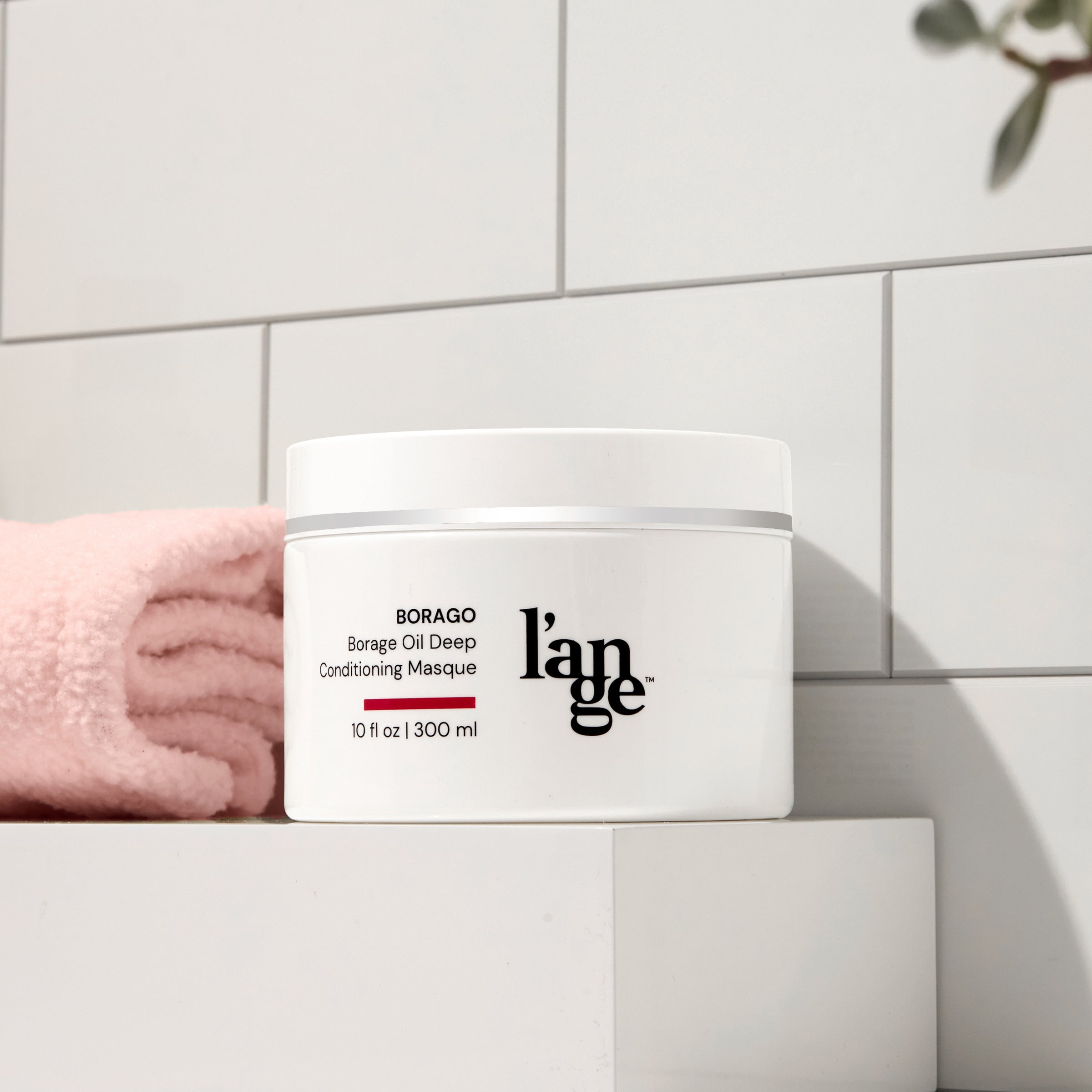 L’ange Borago Borage Oil Deep Conditioning Masque placed on a bathroom shelf next to a folded pink towel.