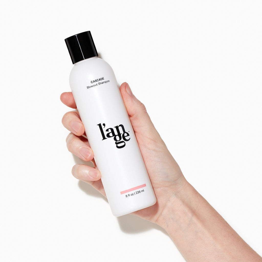 White Cascade Blowout Shampoo bottle with black L’ange logo held by light skinned hand