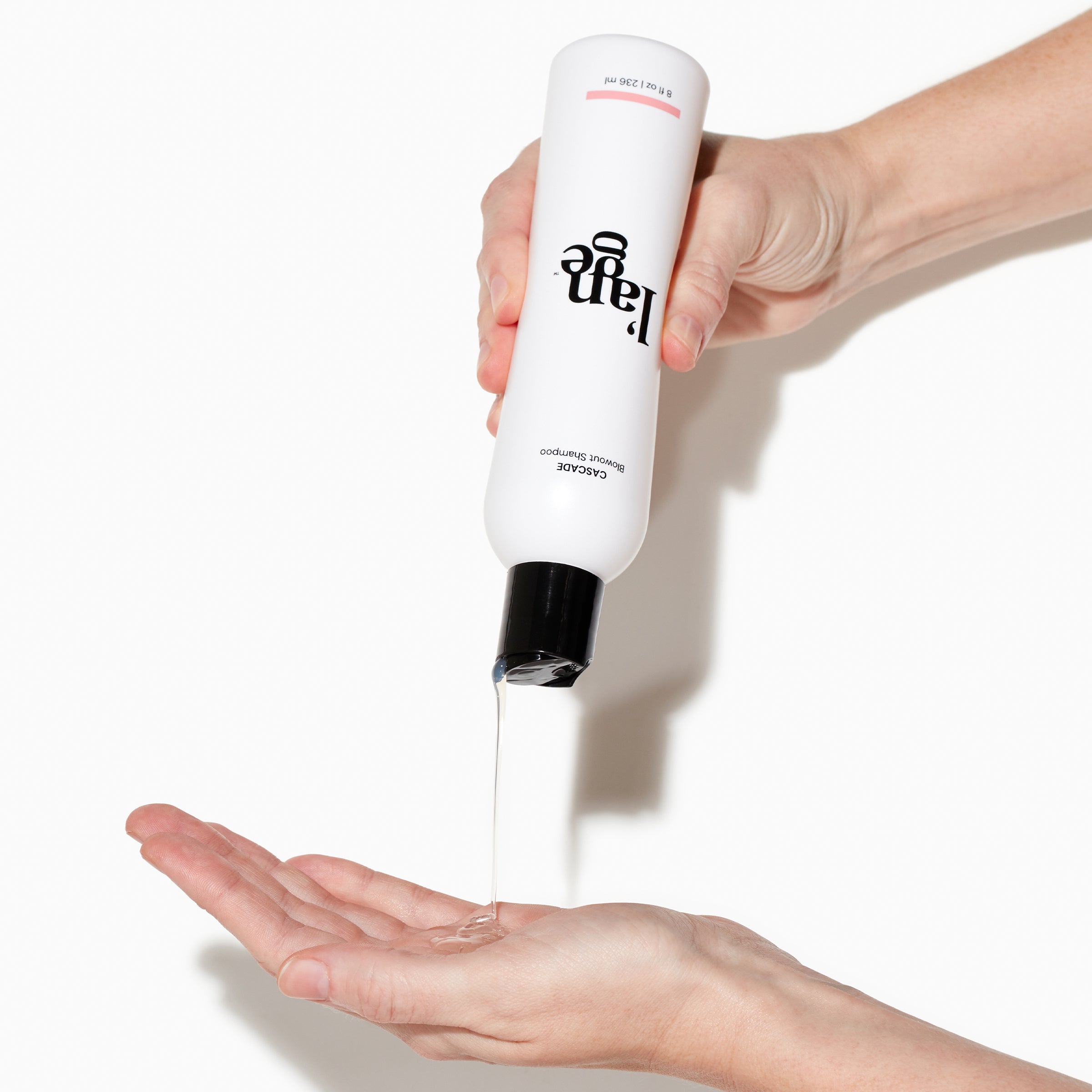 White Cascade Blowout Shampoo bottle with clear shampoo held by two light skinned hands