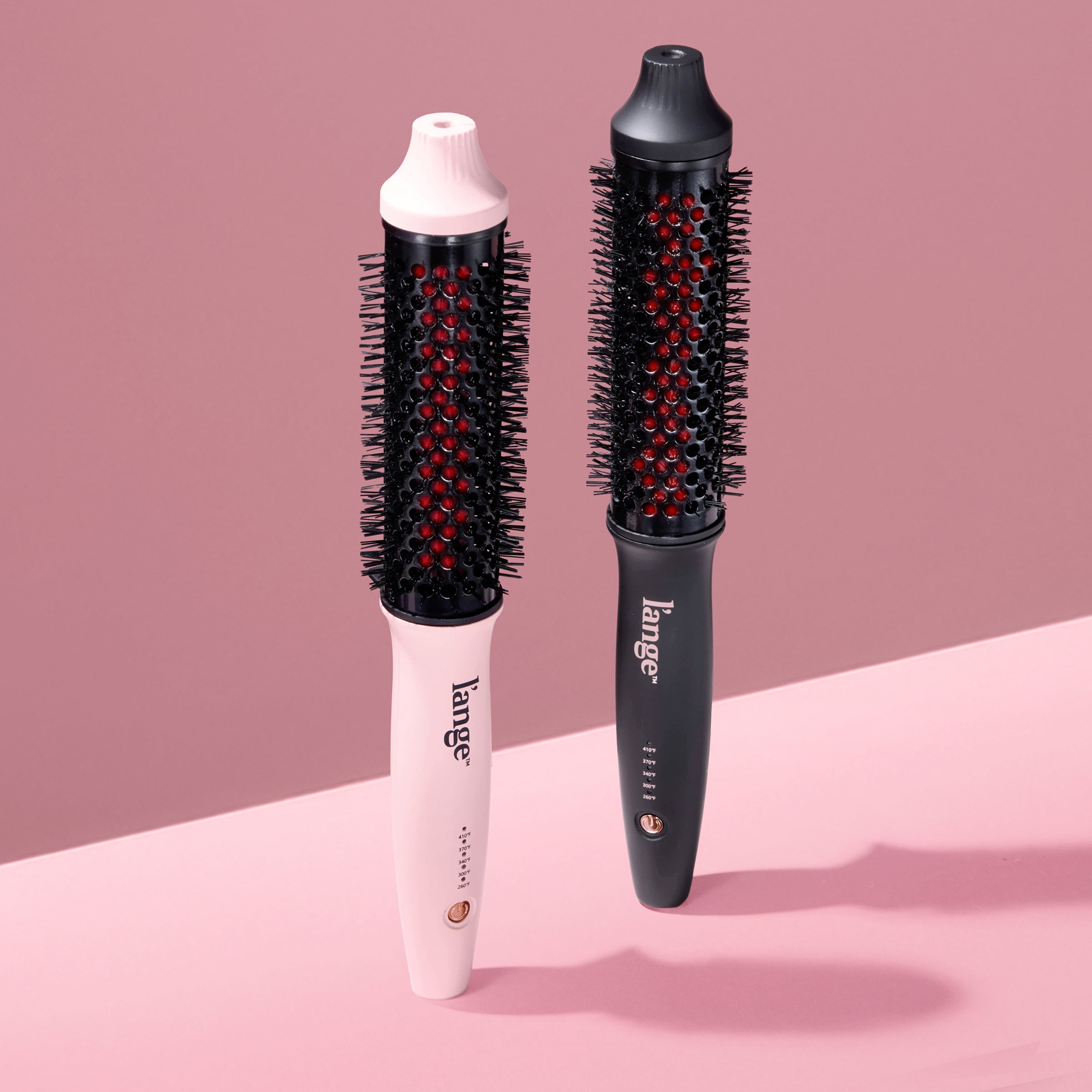 Two L’ange GlamWave heated round brushes in blush pink and matte black on a blush background.
