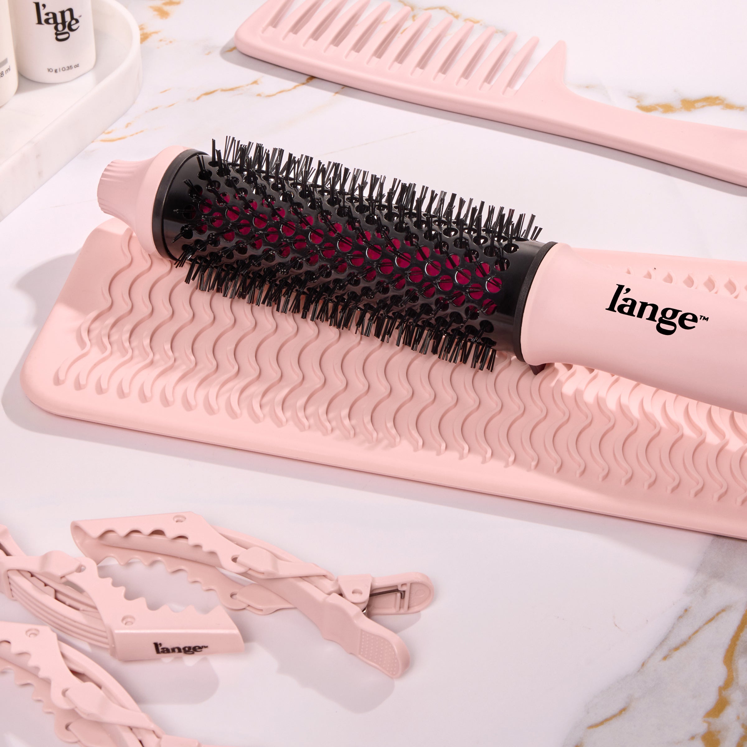 Round thermal brush and sectioning clips with wavy silicone mat in soft pink tones, complemented by styling accessories.