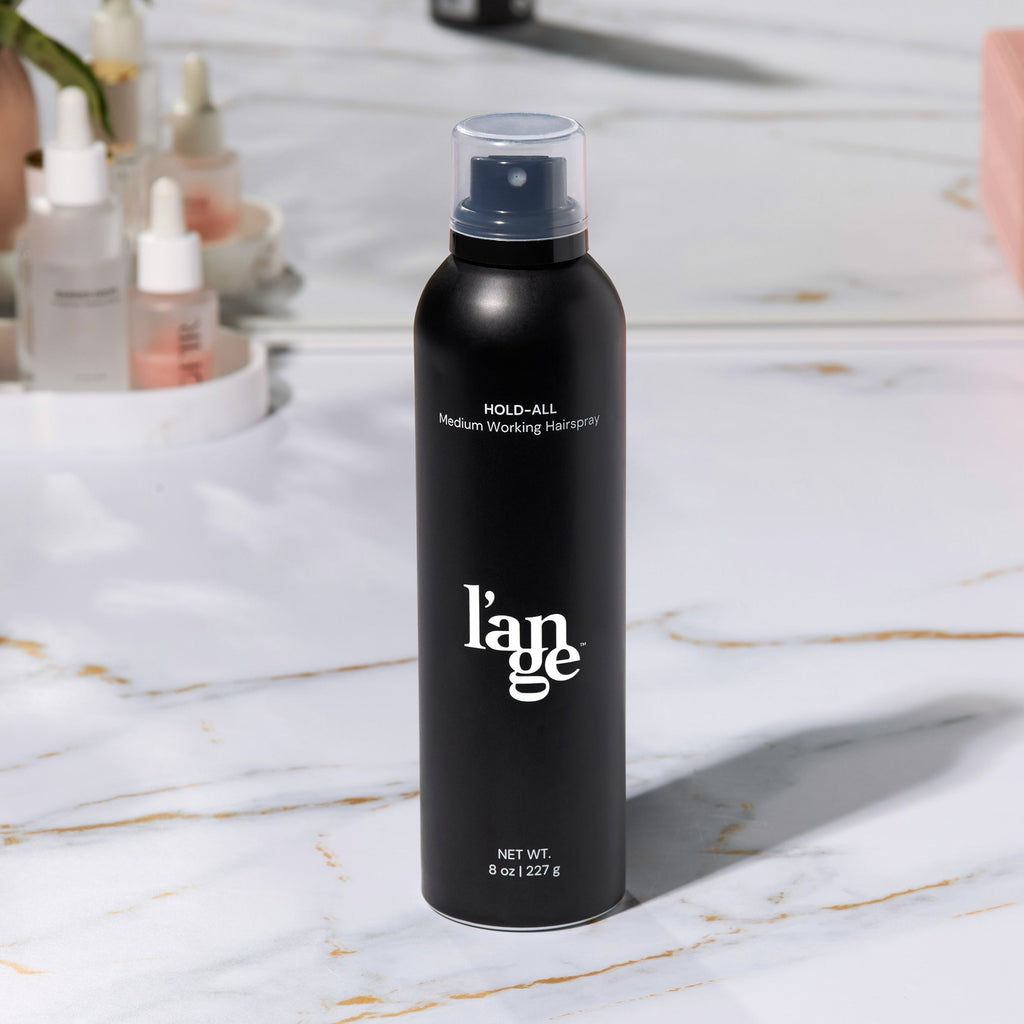 L’ange Hold-All Medium Working Hairspray can on a marble vanity with skincare products in the background.