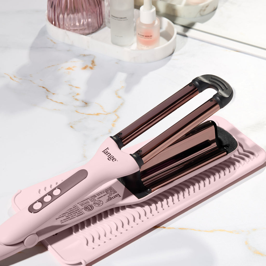 Blush L’ange hair waver resting on a heat-resistant mat on a marble countertop.