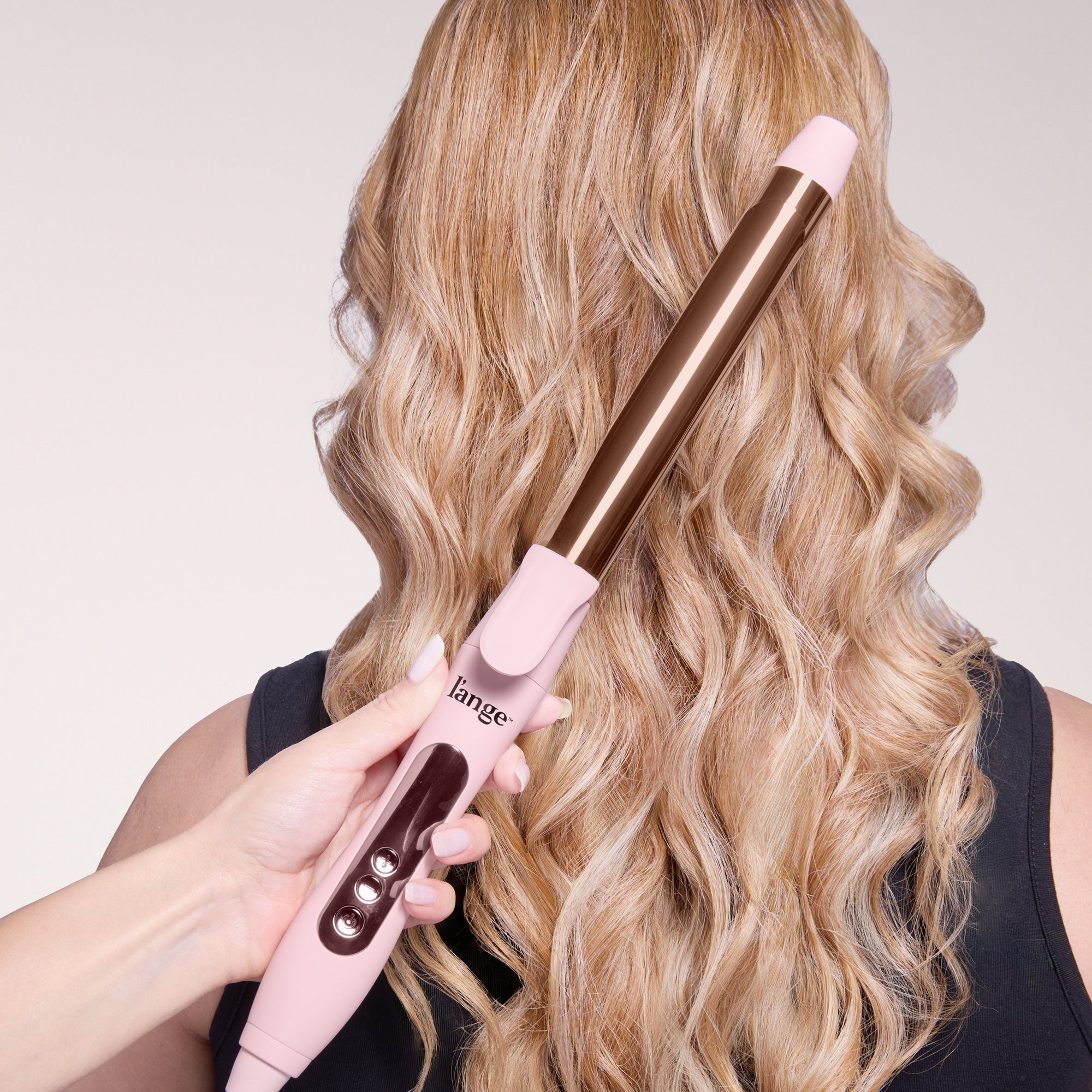 Back of a model’s head with curls, and a hand holding a curling iron in front, showcasing the tool used to create the tousled look and curls.
