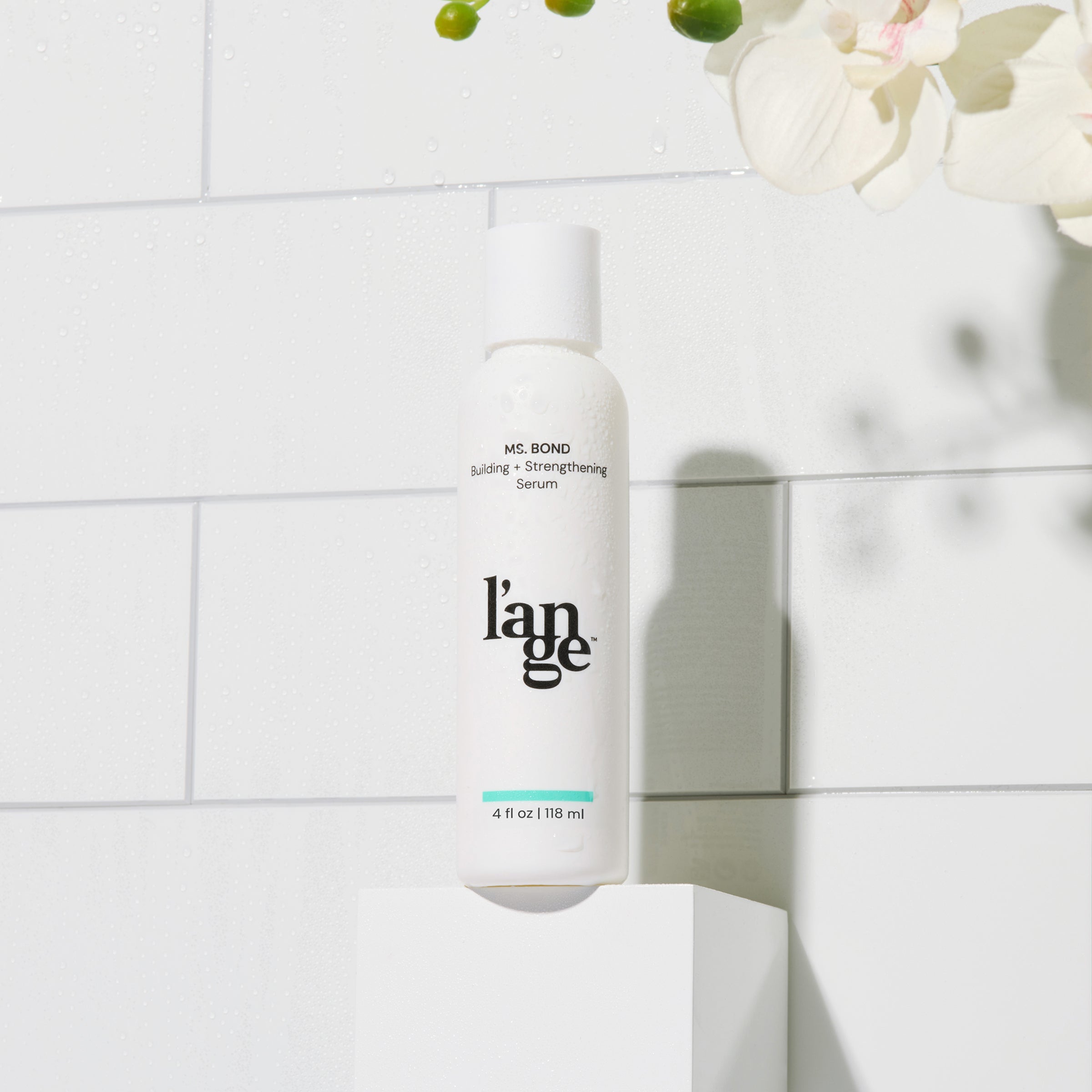 L'ange MS. BOND Building and Strengthening Serum, 4 fl oz (118 ml), displayed in a sleek white bottle against a tiled background with delicate greenery and orchids.