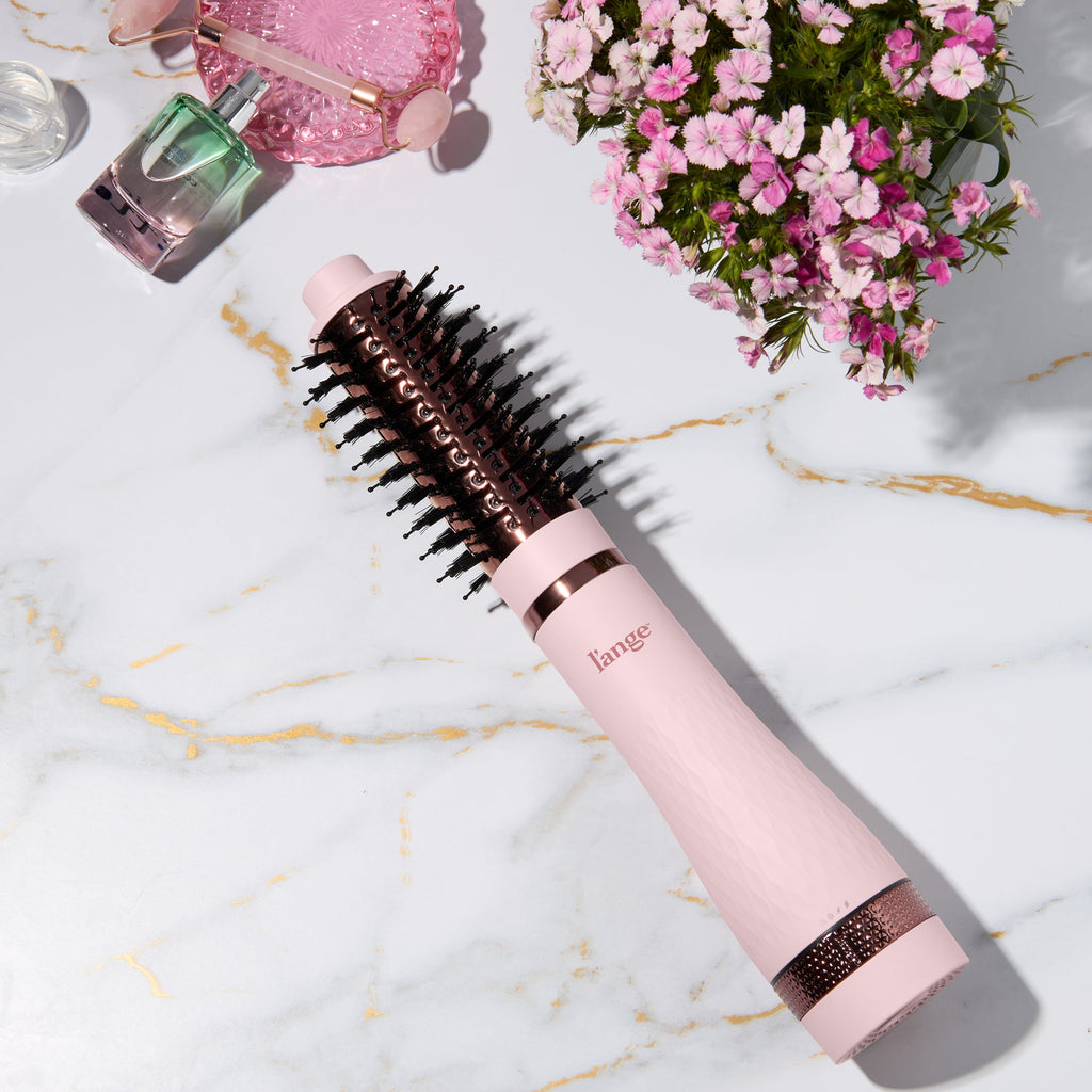 Blush and rose gold L’ange round brush styling tool on a marble surface with flowers and beauty items. 43MM