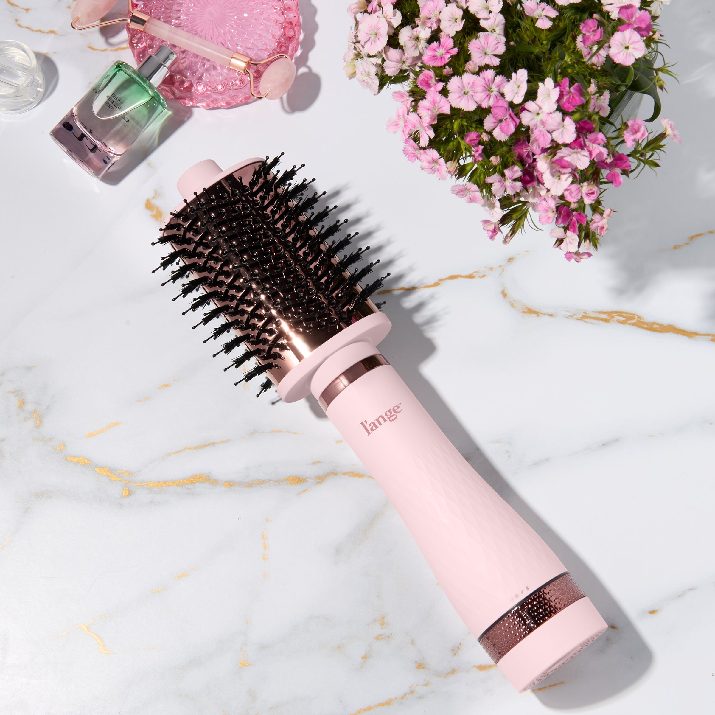 Blush and rose gold L’ange round brush styling tool on a marble surface with flowers and beauty items. 75MM