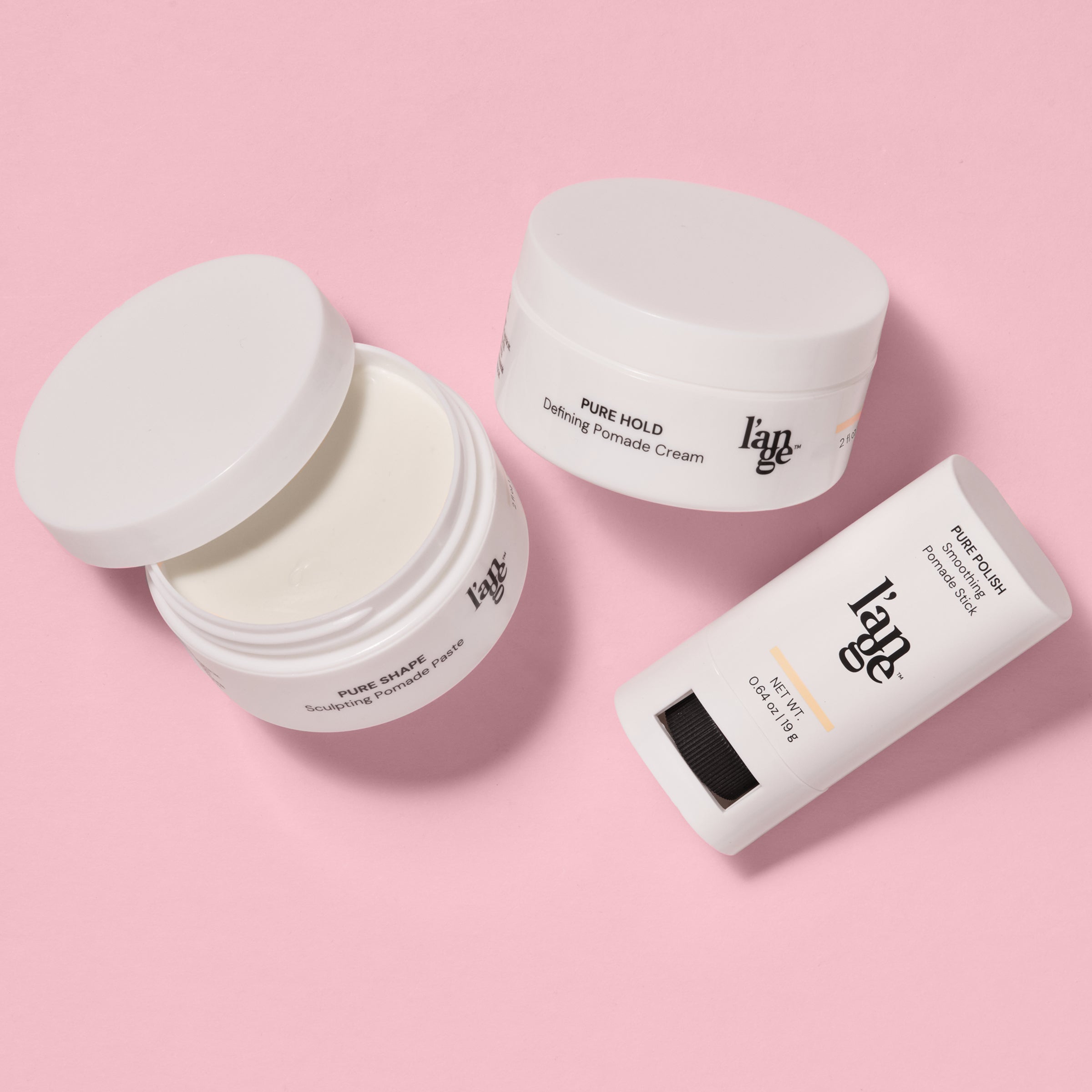 L’ange pomade collection displayed on a pink background, featuring Pure Shape Sculpting Pomade Paste in an open jar, Pure Hold Defining Pomade Cream in a closed jar, and Pure Polish Smoothing Pomade Stick.