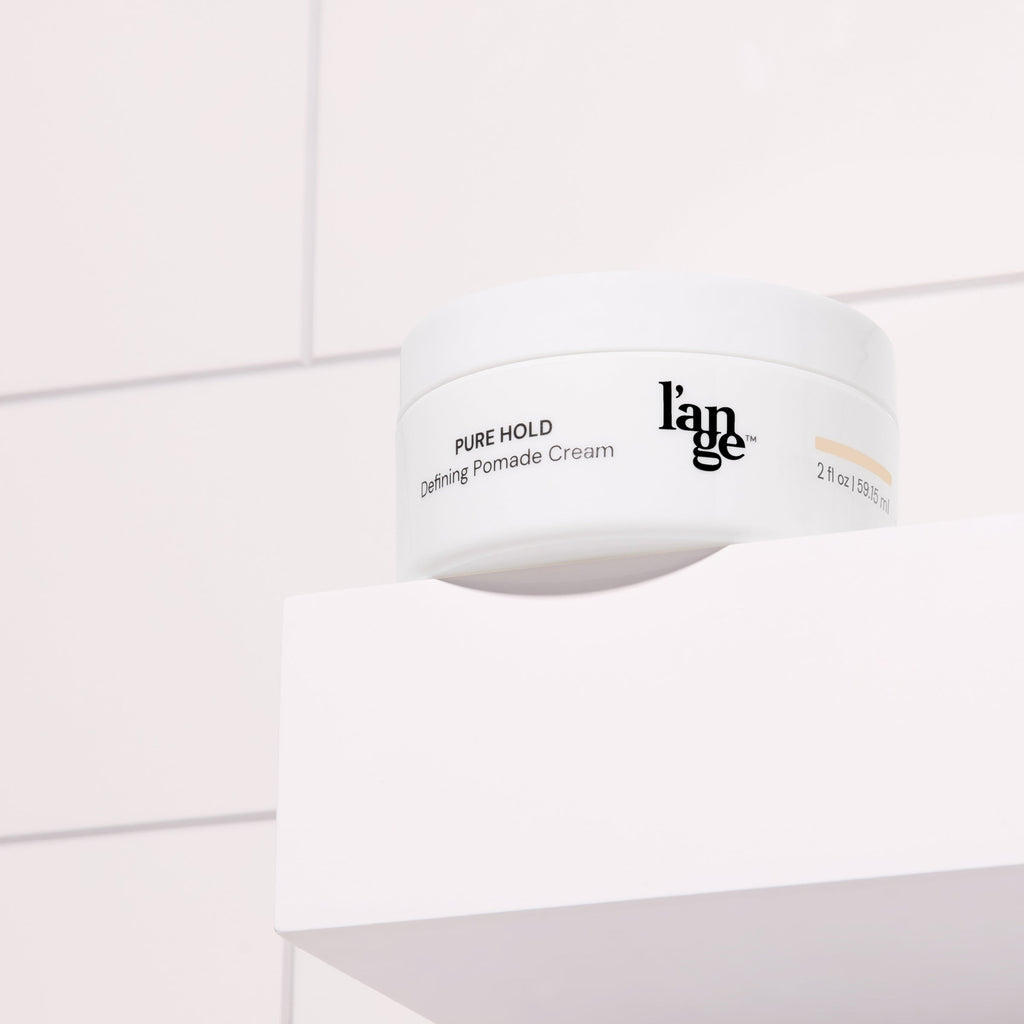 Defining Pomade Cream in a white round jar, placed on a white bathroom shelf with tile background