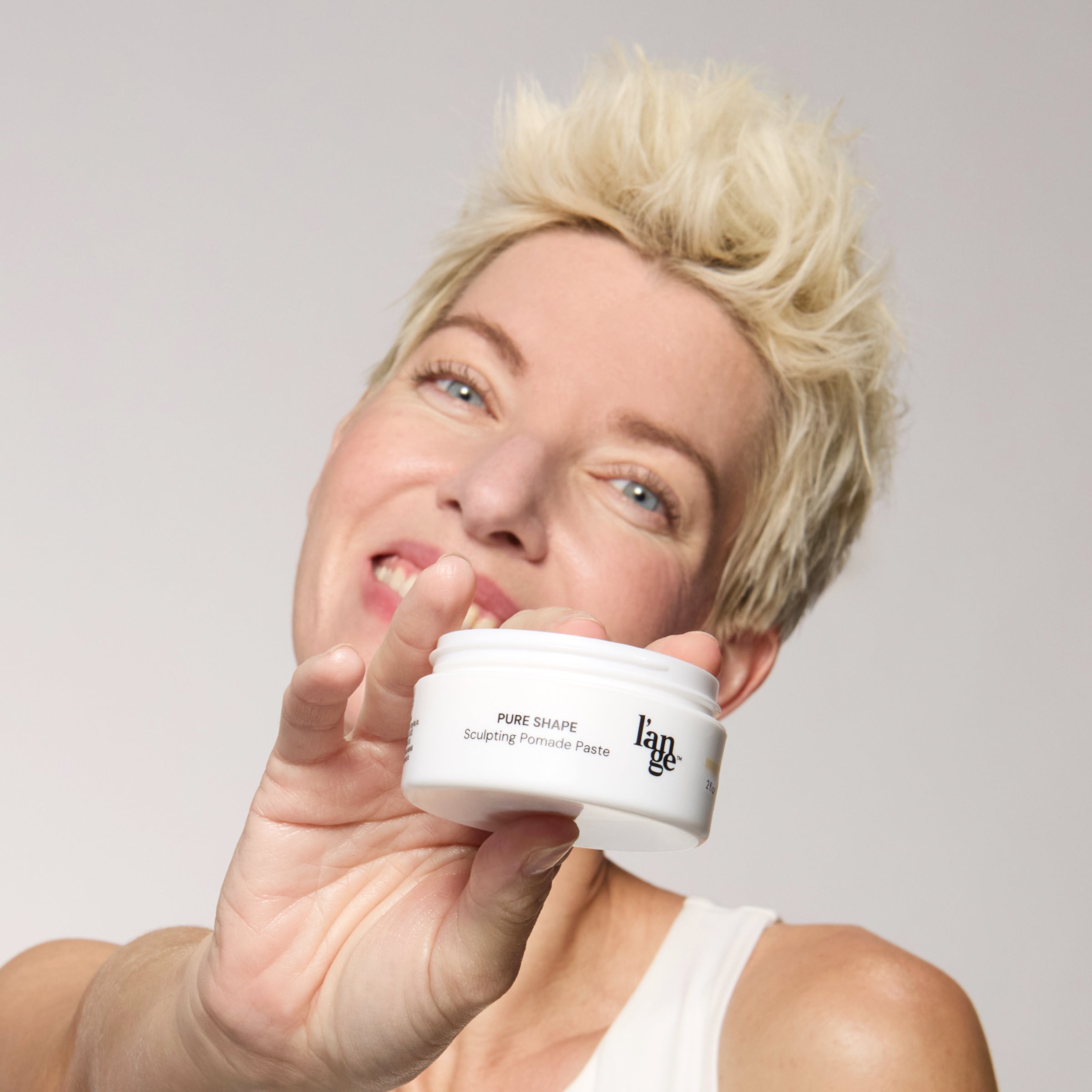woman holding pomade paste jar towards the camera with a neat hair style