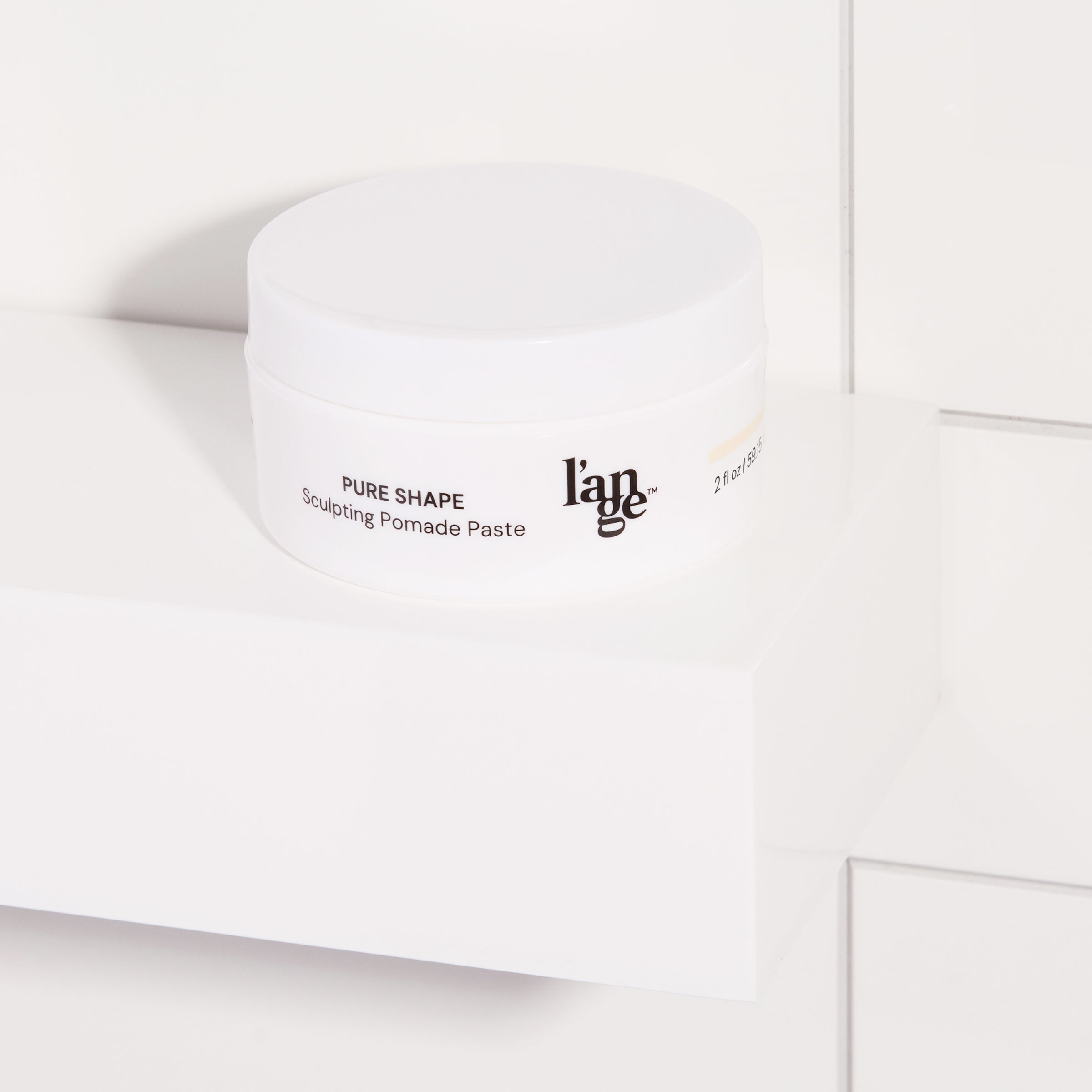 Sculpting Pomade Paste in a white round jar displayed on a bathroom shelf with tile background