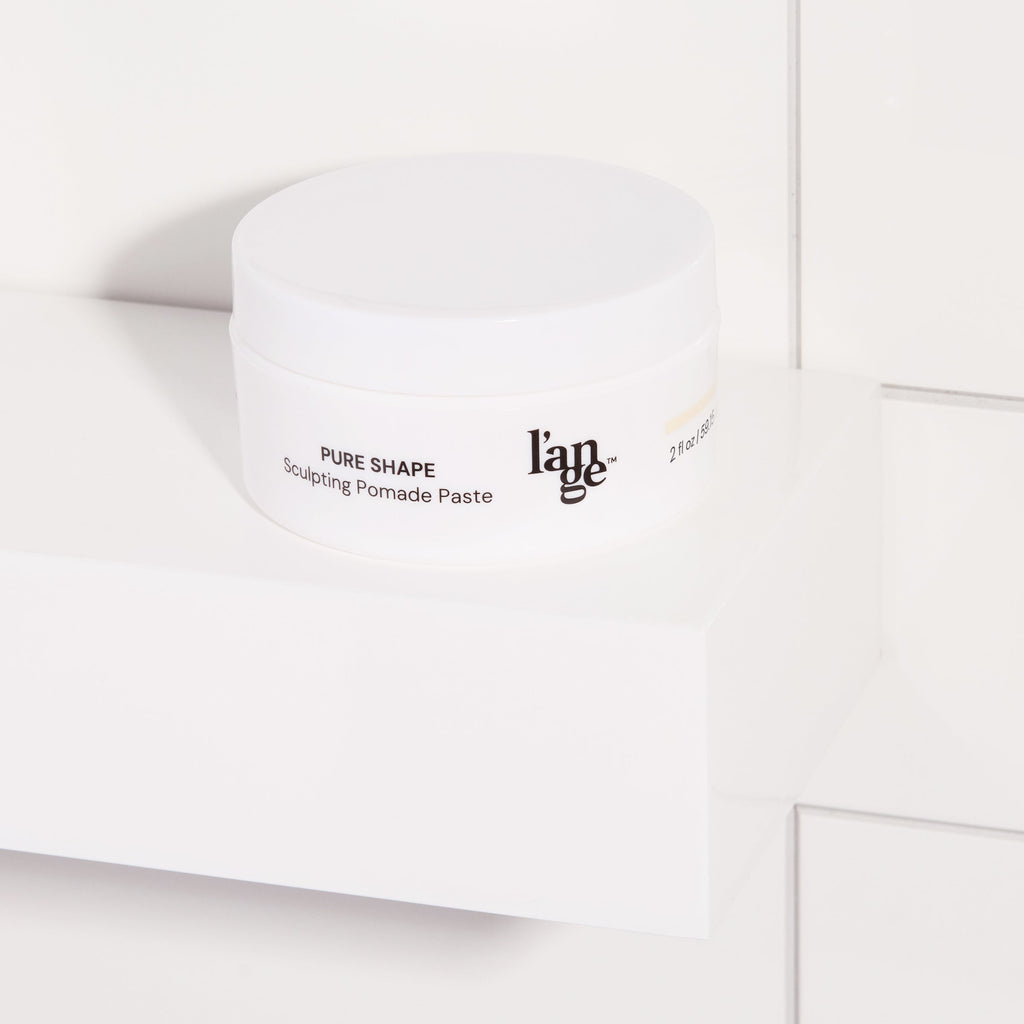 Sculpting Pomade Paste in a white round jar displayed on a bathroom shelf with tile background