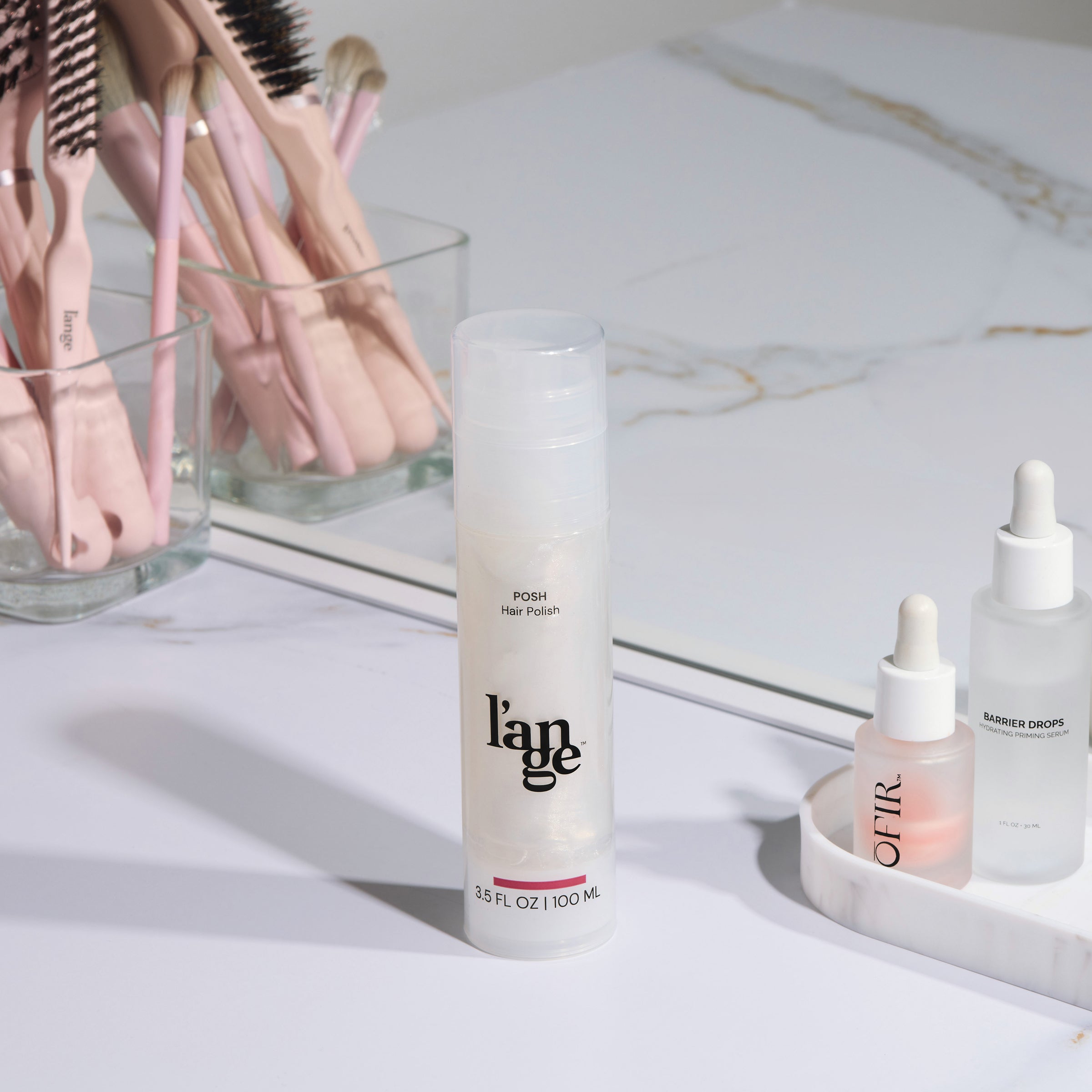 L’ange Posh Hair Polish bottle on a vanity counter with makeup brushes and skincare products.