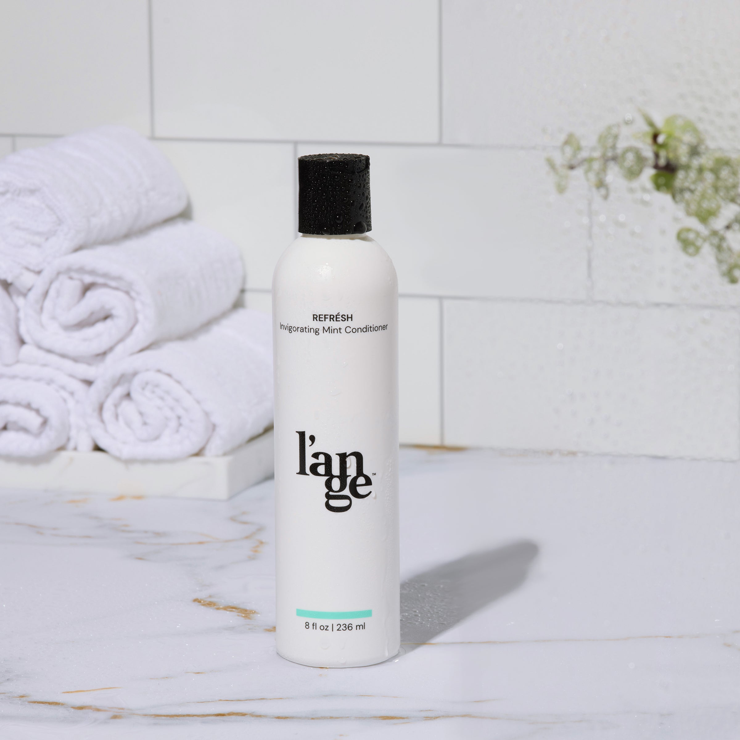 L’ange Refresh Invigorating Mint Conditioner bottle on a marble bathroom counter with white towels and eucalyptus in the background.