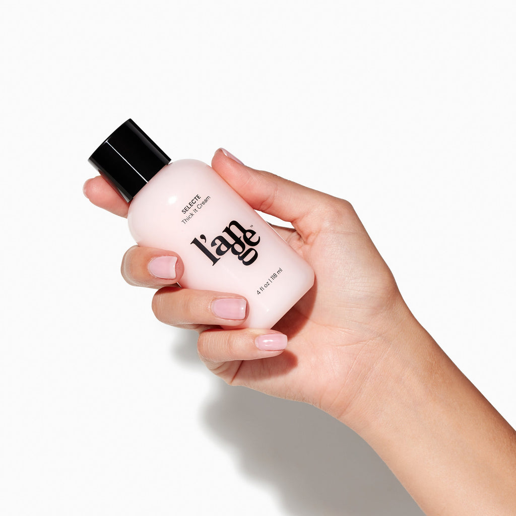Clear 4fl oz bottle of pink Selecte Thick It Cream held by light skinned hand