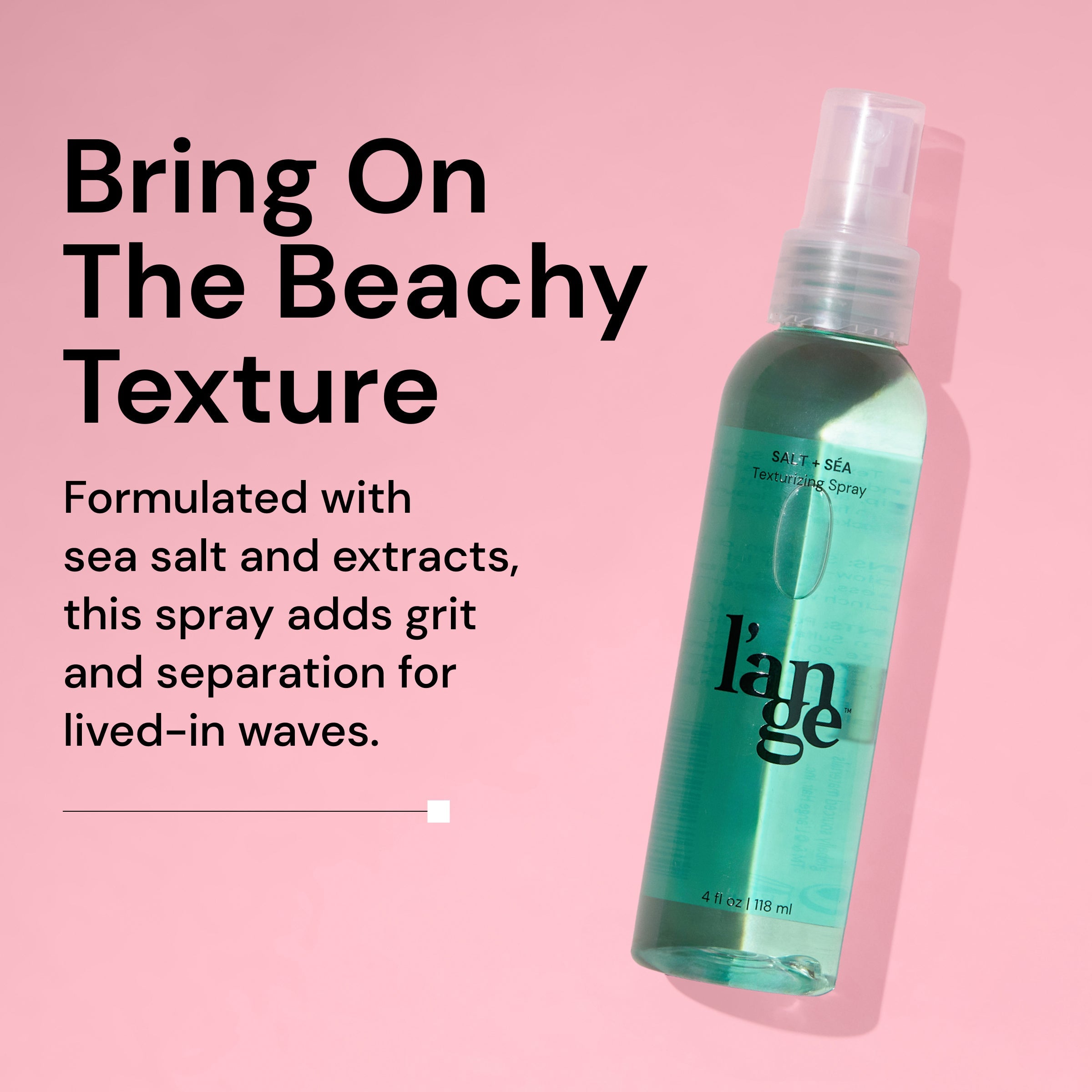 A green bottle of L’ange Salt + Séa Texturizing Spray leans diagonally against a pink background, casting a shadow. Bold text reads: 'Bring On The Beachy Texture.' Below it says: 'Formulated with sea salt and extracts, this spray adds grit and separation for lived-in waves.