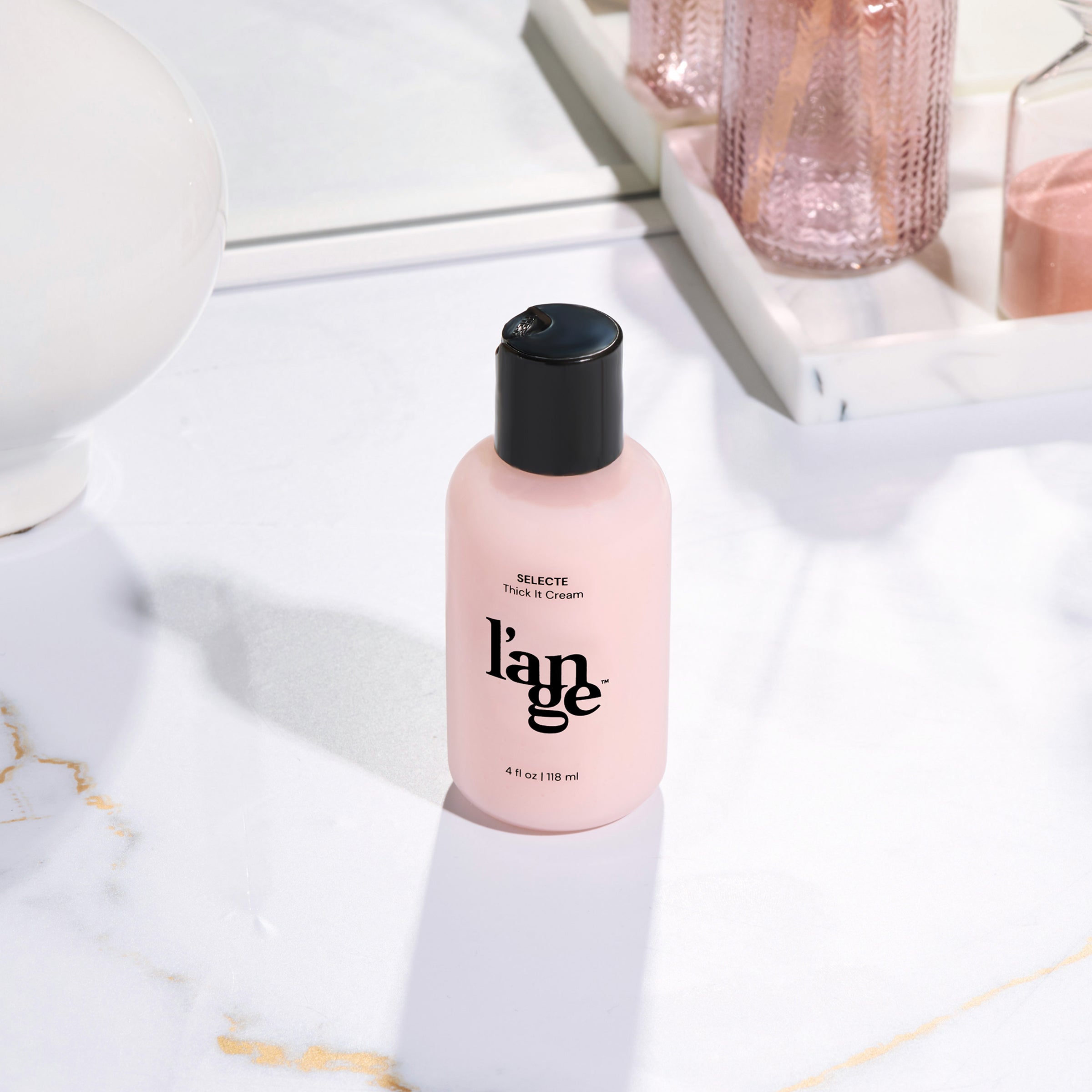 L’ange Selecte Thick It Cream bottle on a marble surface with decorative items in the background.