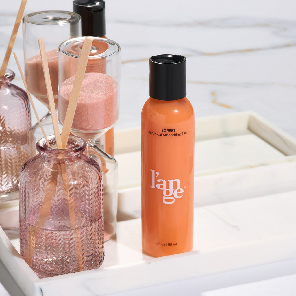 L’ange Sorbet Botanical Smoothing Balm displayed on a white tray with decorative glass bottles and an hourglass.