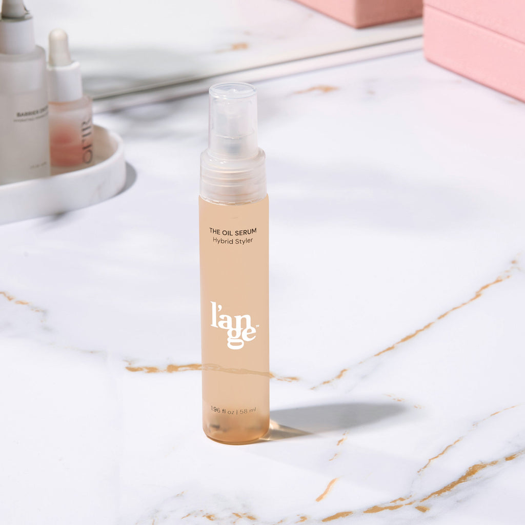L’ange The Oil Serum Hybrid Styler bottle displayed upright on a bathroom counter with a soft-focus background, highlighting its ingredient list and elegant packaging.