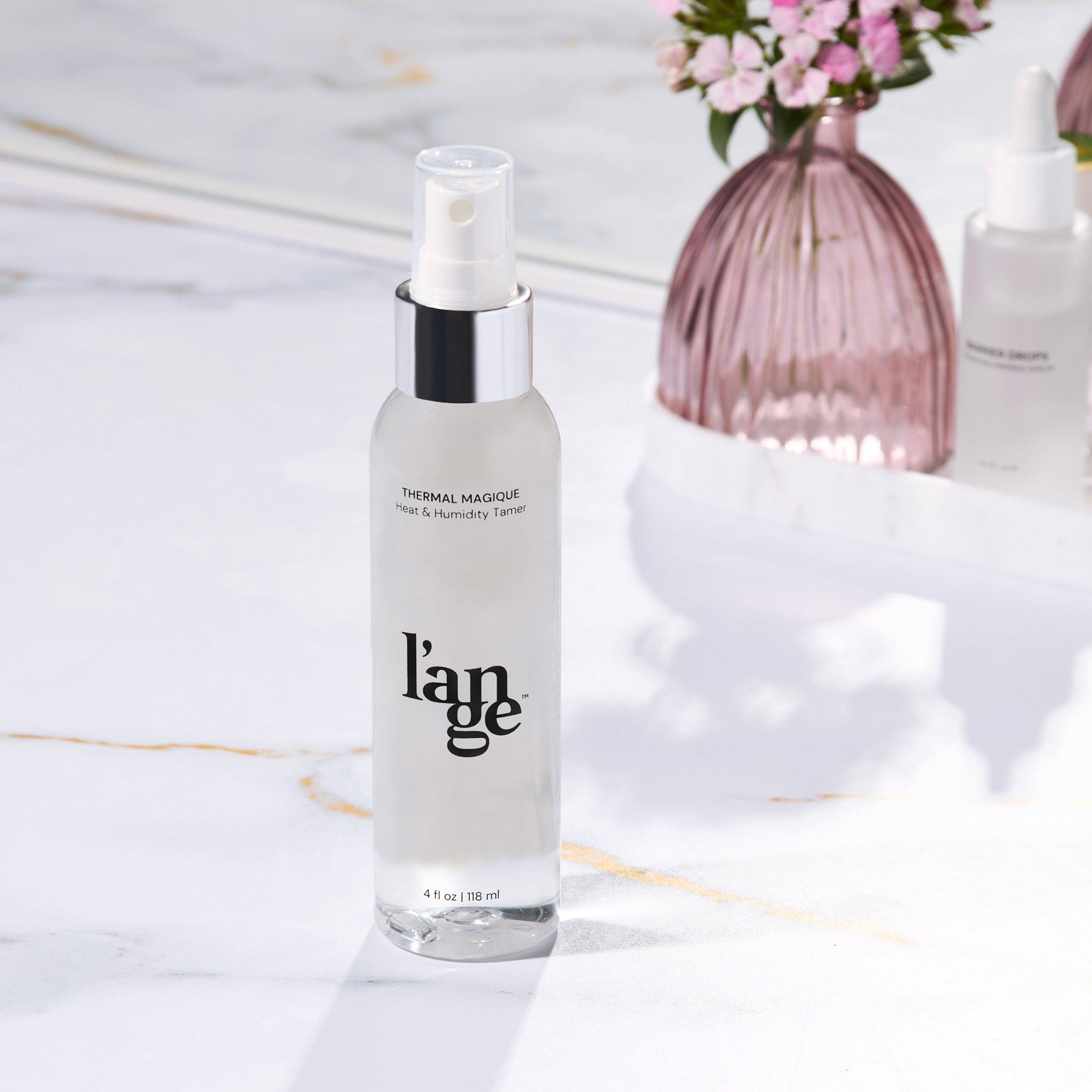 L’ange Thermal Magique heat and humidity tamer bottle on a marble surface with a vase and mirror in the background.