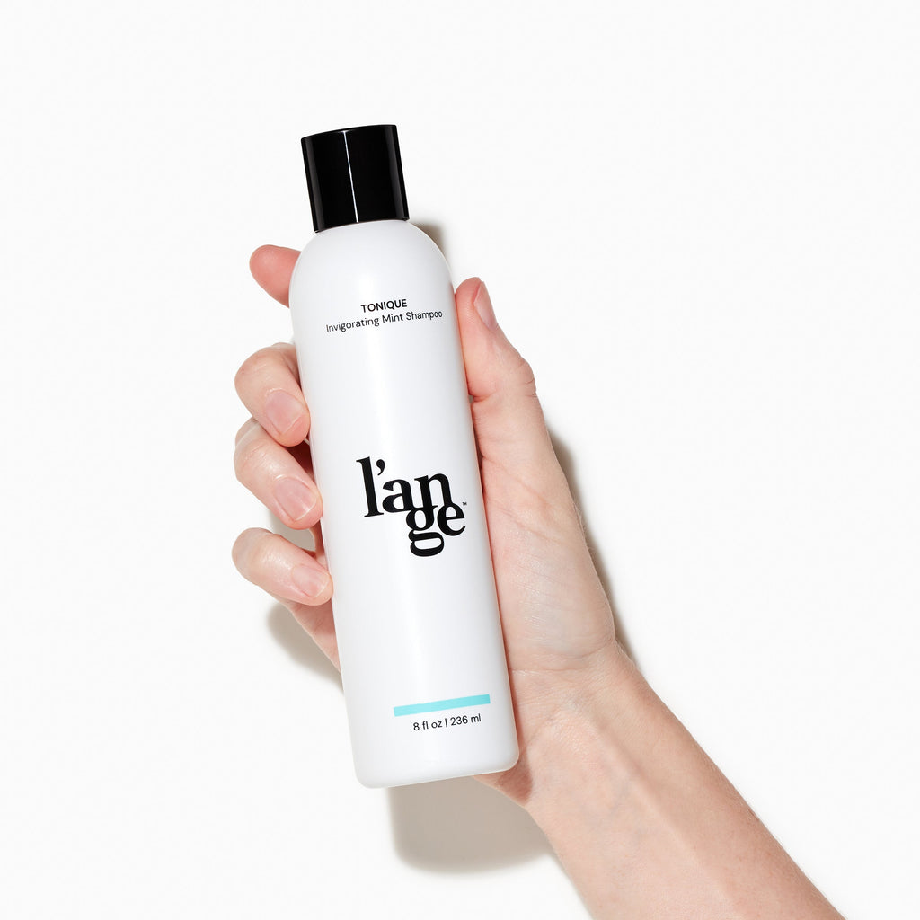 White Tonique Invigorating Mint Shampoo bottle held by light skinned hand