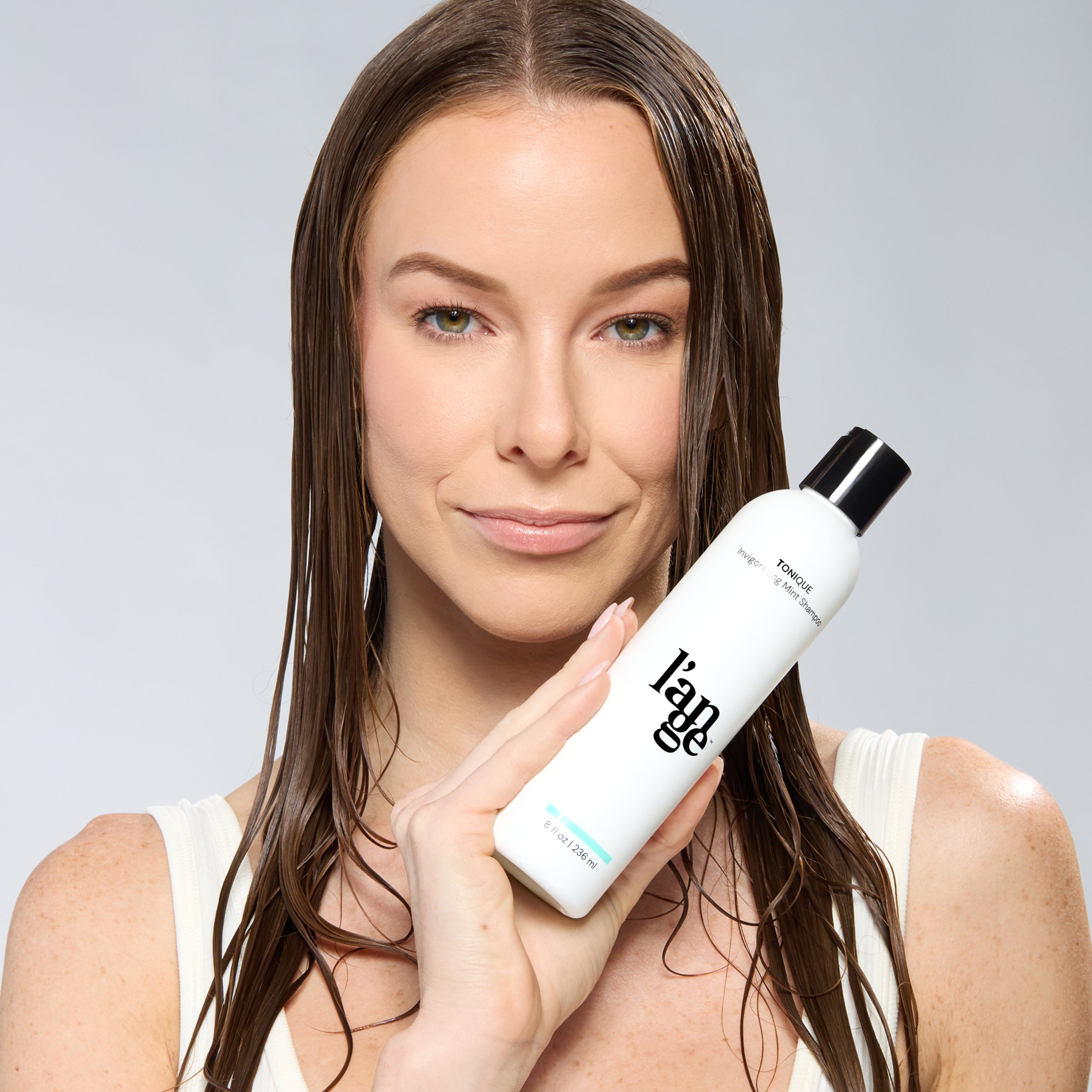 Woman with wet hair holding a bottle of L’ange Tonique hair product.