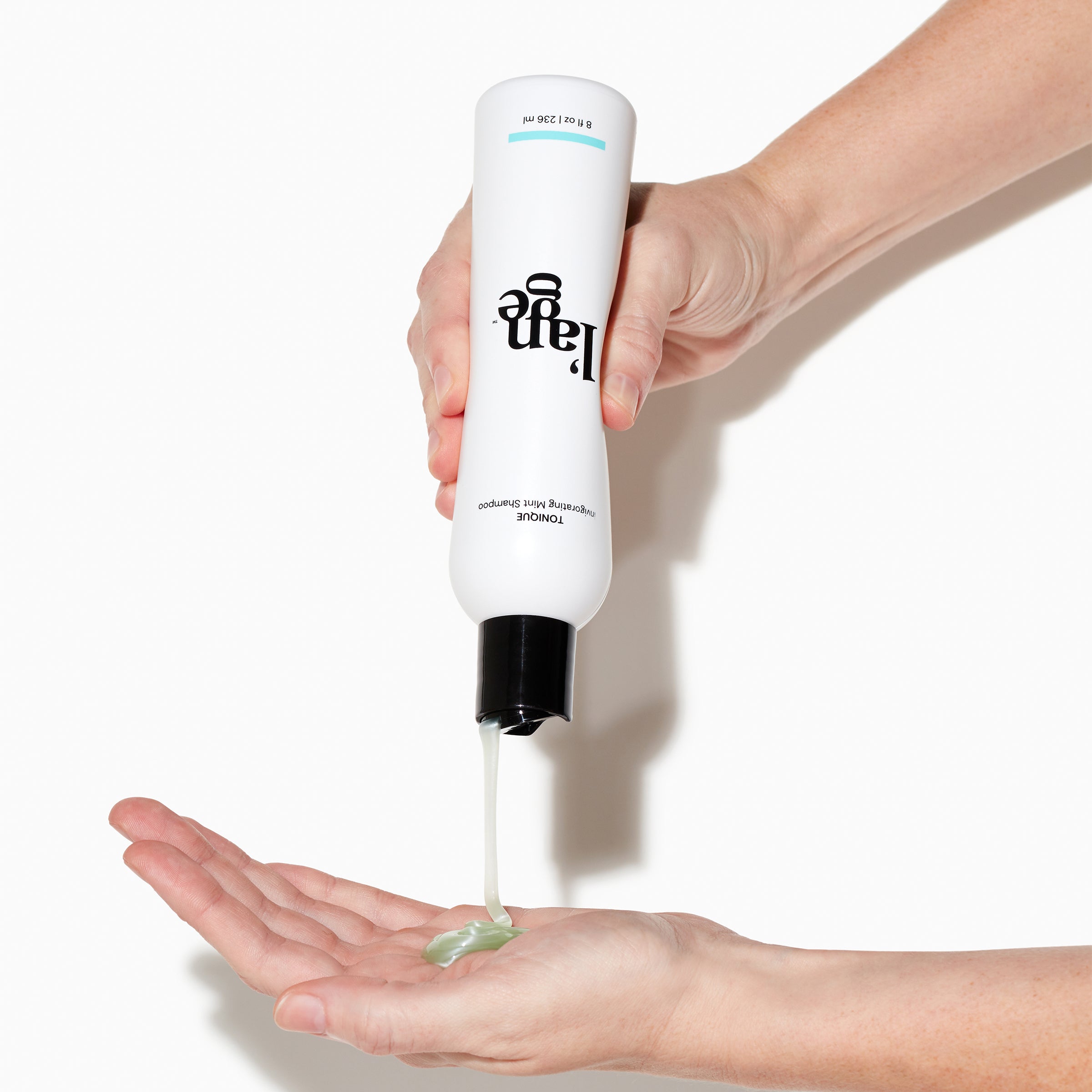 White Tonique Invigorating Mint bottle with light green shampoo held by two light skinned hands